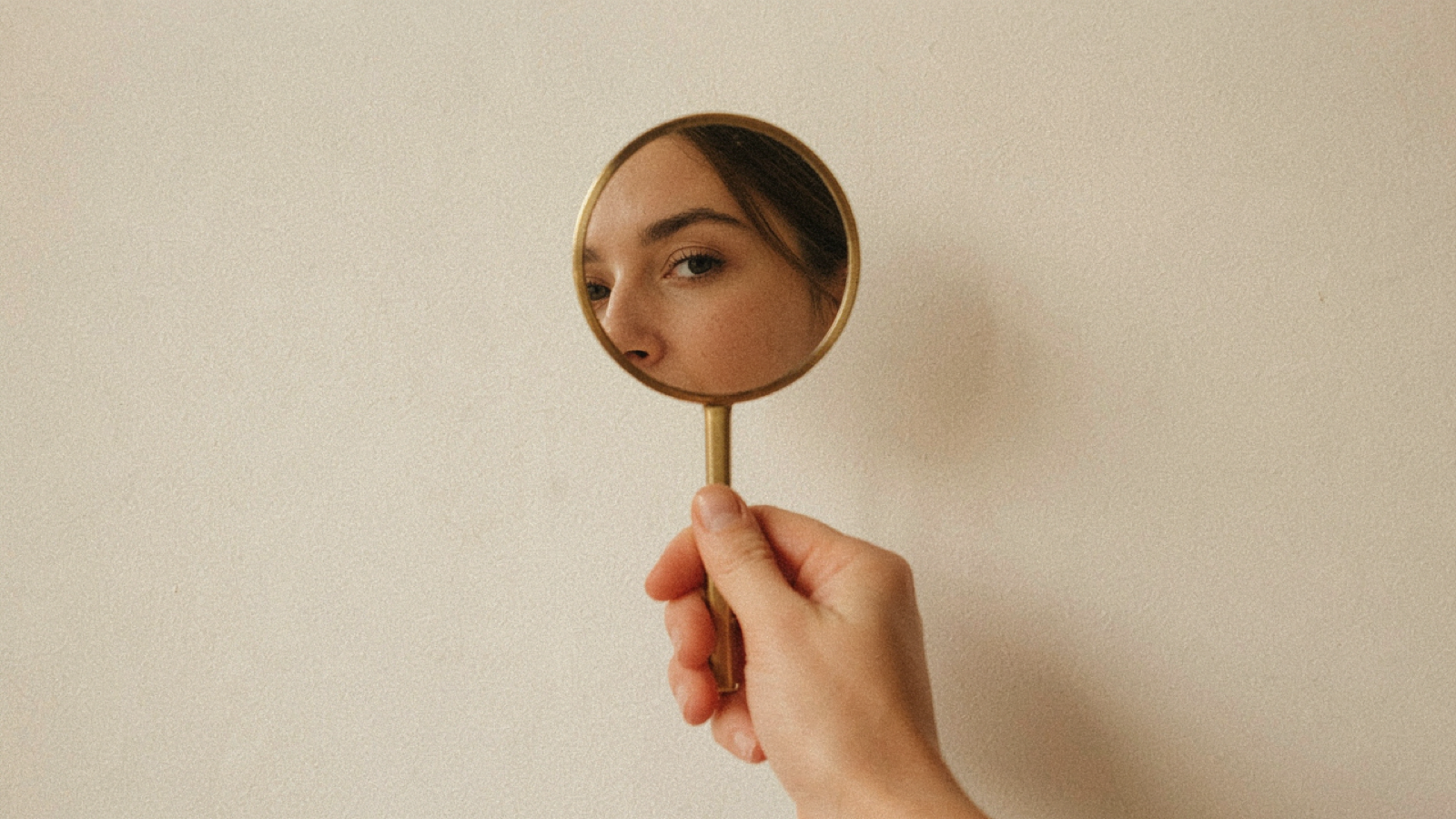 A hand holding a round mirror reflecting a softly lit half face